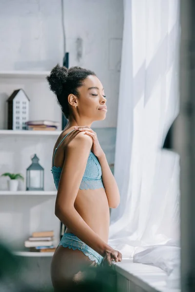 Hermosa tierna afroamericana chica en lencería posando en dormitorio cerca de ventana - foto de stock