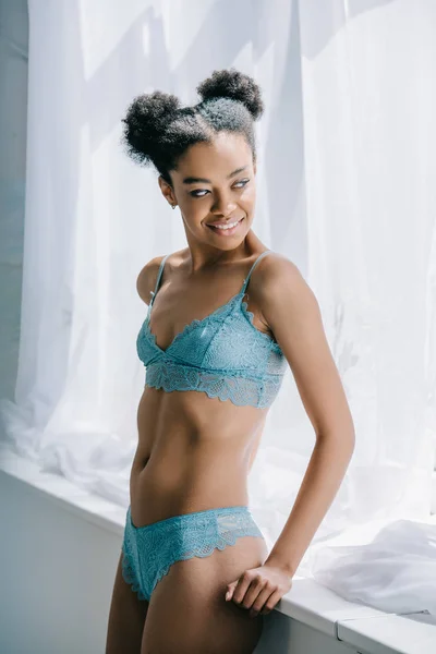 Attractive young african american woman in blue lingerie posing near window — Stock Photo