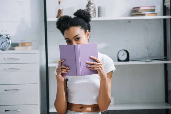 Atractivo africano americano mujer estudiante con libro mirando cámara - foto de stock