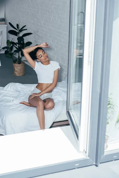 Attraente giovane donna seduta sul letto al mattino a casa — Foto stock