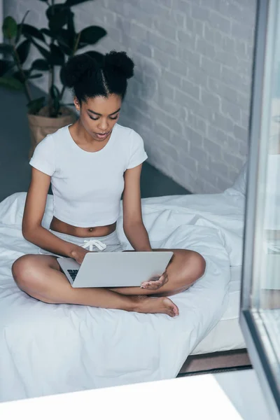 Focused young woman working with laptop on bed at home — Stock Photo