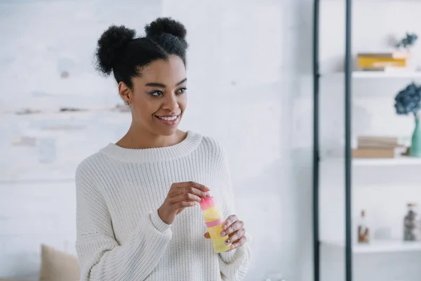 Sorridente giovane donna con bolle di sapone a casa guardando altrove — Foto stock