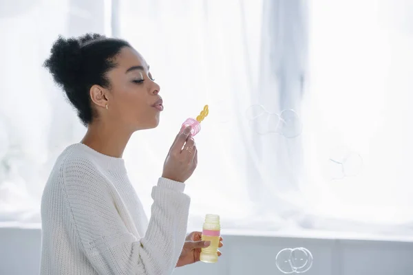 Side view of attractive young woman blowing soap bubbles at home — Stock Photo