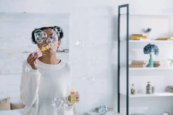 Attraente giovane donna soffiando bolle di sapone a casa — Foto stock