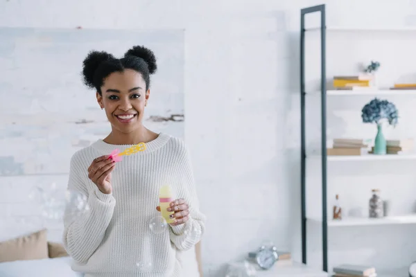 Giovane donna sorridente con bolle di sapone a casa — Foto stock