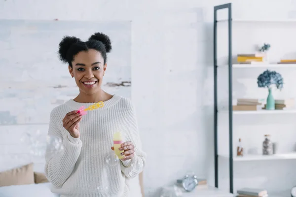 Smiling young woman with soap bubbles at home — Stock Photo