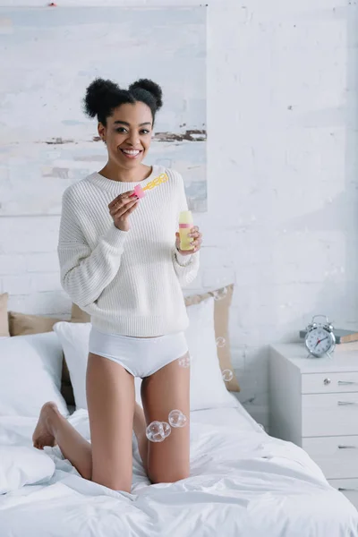 Schöne junge Frau mit Seifenblasen, die zuhause auf dem Bett steht — Stockfoto