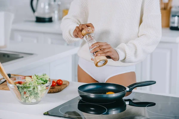 Обрезанный снимок женщины, приправляющей куриное яйцо на сковороде на кухне — стоковое фото