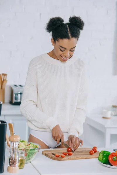 Giovane donna sorridente che affetta pomodori per insalata a cucina — Foto stock