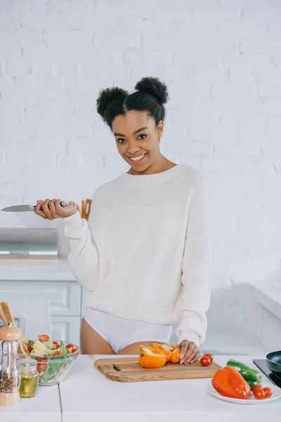 Glückliche junge Frau schneidet Gemüse für das Frühstück in der Küche und blickt in die Kamera — Stockfoto