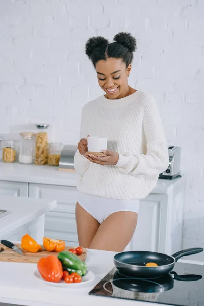 Hermosa joven con taza de café preparando el desayuno en casa - foto de stock