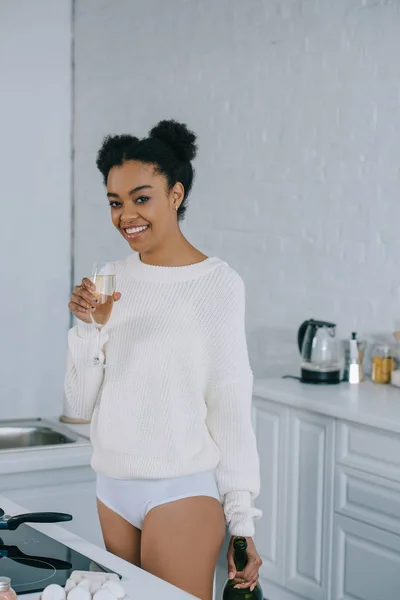 Smiling young woman with glass of champagne at kitchen — Stock Photo