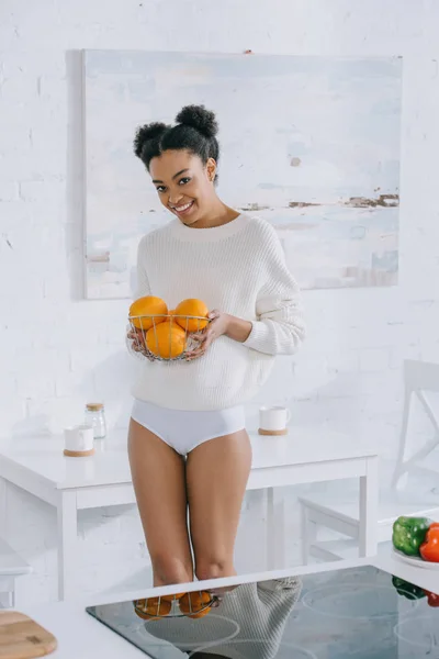 Smiling young woman with basket of fresh oranges at home — Stock Photo