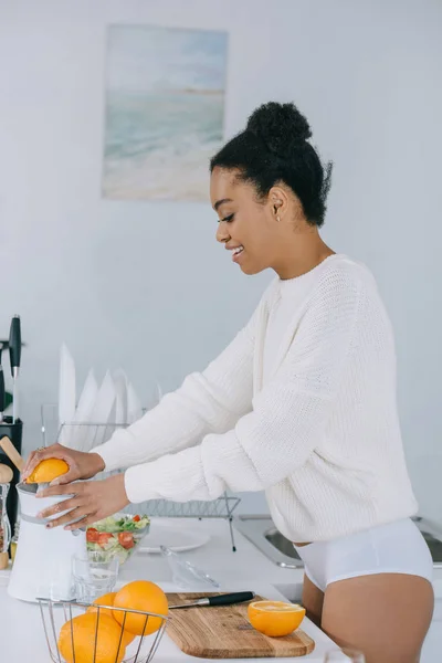 Happy young woman squeezing fresh orange juice at kitchen — Stock Photo