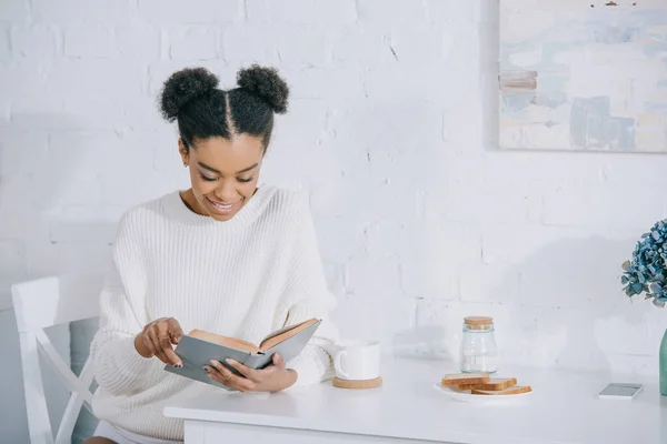 Belle jeune femme lecture livre pendant la pause café à la maison — Photo de stock