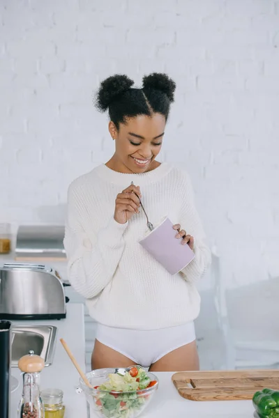 Счастливая молодая женщина ест мороженое из ведра на кухне — стоковое фото