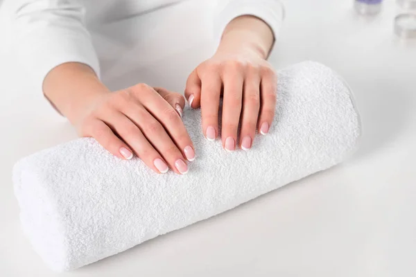 Imagen recortada de la mujer cogida de la mano para el procedimiento de manicura en la mesa con toalla en el salón de belleza - foto de stock