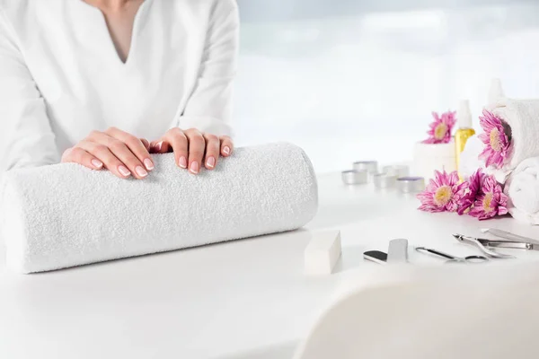 Image recadrée de femme tenant la main à table avec des serviettes, des fleurs, des bougies, des bouteilles d'huile d'arôme et des instruments pour la manucure dans un salon de beauté — Photo de stock