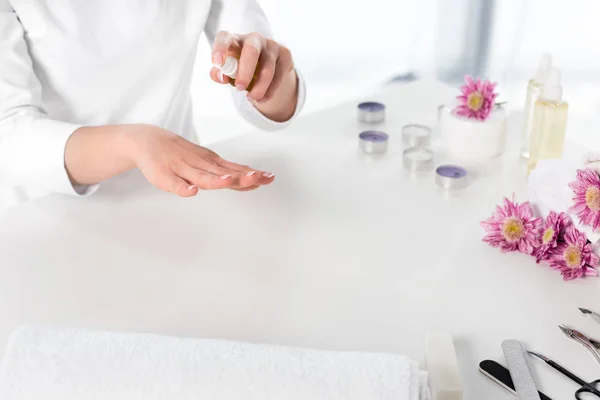 Vue partielle de la femme en utilisant l'huile aromatique à table avec des serviettes, des fleurs, des bougies et des instruments pour la manucure dans le salon de beauté — Photo de stock