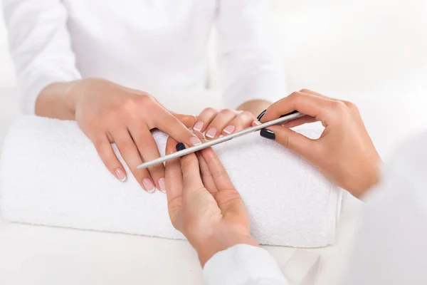 Partial view of woman receiving manicure by beautician with nail file at table with towel in beauty salon — Stock Photo