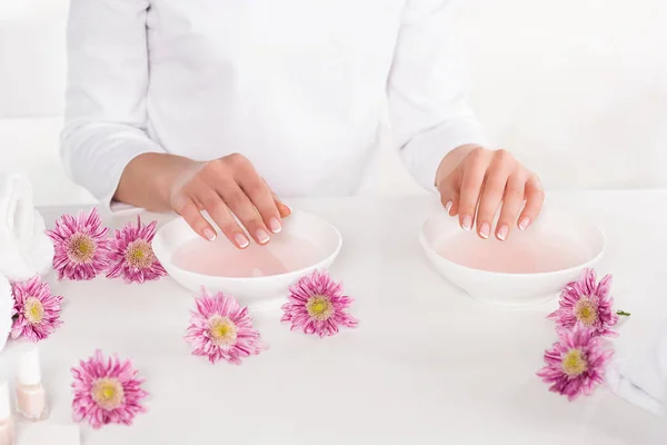 Teilansicht einer Frau, die im Schönheitssalon ein Bad für Nägel am Tisch mit Blumen, Handtüchern und Nagellacken erhält — Stockfoto