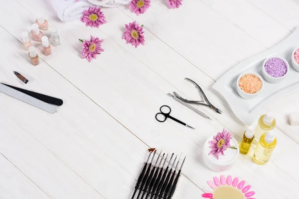 Elevated view of flowers, nail polishes, nail files, scissors, cuticle pusher, nail clippers, aroma oil bottles, sea salt, cream, tools for manicure and samples of nail varnishes at table — Stock Photo