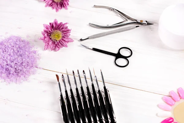 Close up shot of colorful sea salt, instruments for manicure, flowers, nail polishes, cream container, nail clippers, cuticle pusher and samples of nail varnishes for manicure and pedicure at table in beauty salon — Stock Photo