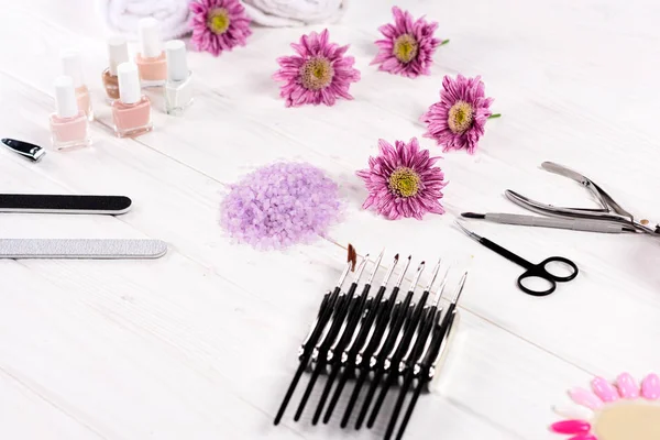 Close up shot of colorful sea salt, towels, flowers, nail polishes, scissors, nail clippers, cuticle pusher, nail files and samples of nail varnishes for manicure and pedicure at table in beauty salon — Stock Photo