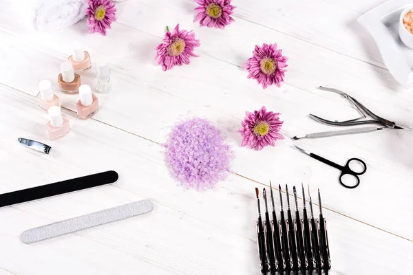 Blick von oben auf buntes Meersalz, Handtücher, Blumen, Nagellacke, Nagelscheren, Nagelhautschieber, Scheren, Nagelfeilen und Instrumente zur Maniküre am Tisch im Schönheitssalon — Stockfoto