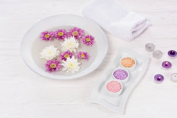 Vista close-up de banho para unhas com flores à mesa com toalha, sal marinho colorido e velas de aroma para manicure e pedicure no salão de beleza — Fotografia de Stock