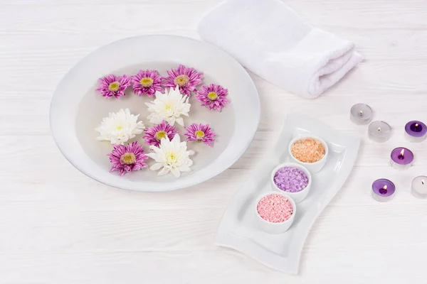 Vue rapprochée du bain pour ongles avec des fleurs à table avec serviette, sel de mer coloré et bougies aromatiques pour manucure et pédicure dans un salon de beauté — Photo de stock