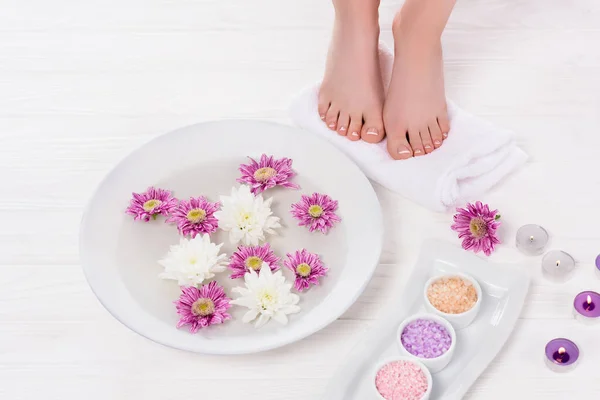 Visão parcial da mulher descalça recebendo banho para unhas com sal marinho colorido e flores perto de velas de aroma no salão de beleza — Fotografia de Stock