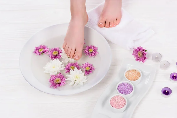 Schnappschuss einer barfüßigen Frau, die im Schönheitssalon ein Nagelbad mit buntem Meersalz und Blumen in der Nähe von Duftkerzen erhält — Stockfoto