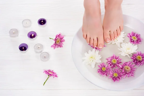 Tiro recortado de mujer descalza recibiendo baño para las uñas flores cerca de velas de aroma en el salón de belleza - foto de stock