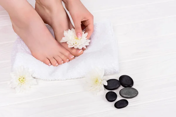 Partial view of barefoot woman on spa treatment with towel, flowers and spa stones — Stock Photo