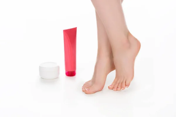 Vue partielle de la femme pieds nus avec des récipients à crème pour les soins de la peau isolé sur fond blanc — Photo de stock