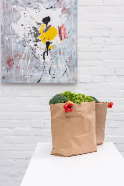 Bolsas de la tienda de comestibles con verduras en la mesa delante de la pared de ladrillo blanco con imagen abstracta - foto de stock