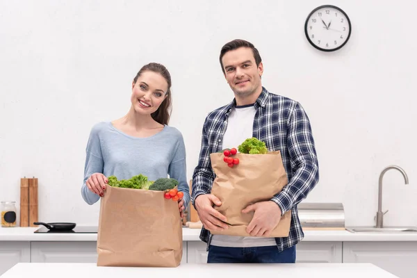 Счастливая пара взрослых с бумажными пакетами из продуктового магазина на кухне — стоковое фото