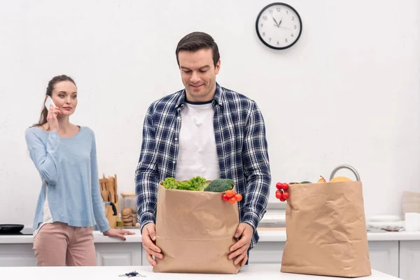 Happy adult man carrying paper bag from grocery store while his wife talking by phone — Stock Photo