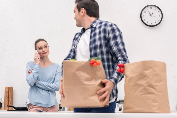 Дорослий чоловік несе паперовий пакет з продуктового магазину, а його дружина розмовляє по телефону — стокове фото
