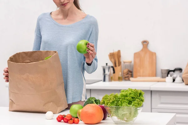 Cropped shot of smiling adult woman taking fruits and vegetables out of paper bag — Stock Photo
