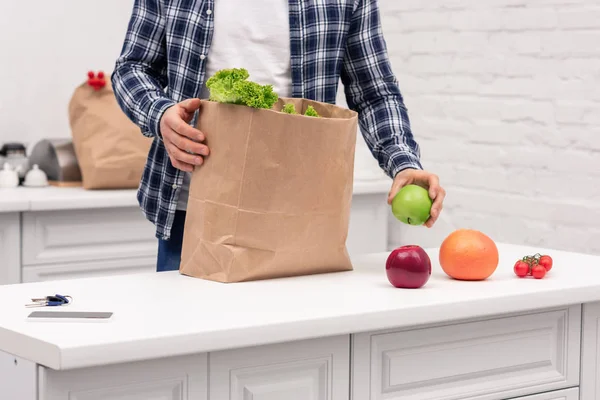 Recortado tiro de hombre desembalaje tienda de comestibles bolsa de papel en la cocina - foto de stock