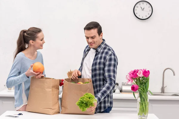 Hermosa pareja de adultos tomando verduras y frutas de bolsas de papel de la tienda de comestibles - foto de stock