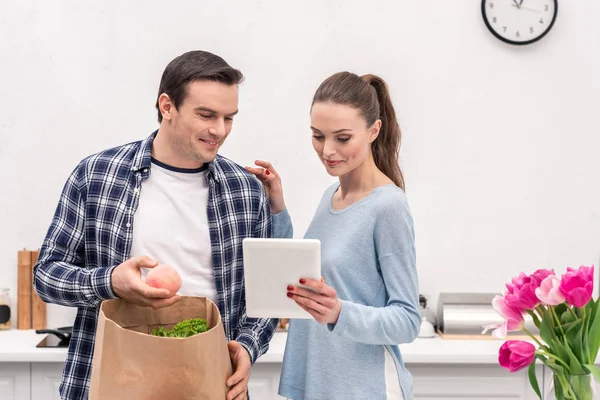 Attraktives erwachsenes Paar überprüft Einkaufsliste nach dem Einkaufen in Tablette — Stockfoto