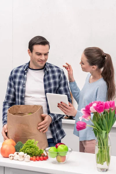 Happy adult couple checking buys list in tablet after grocery shopping — Stock Photo