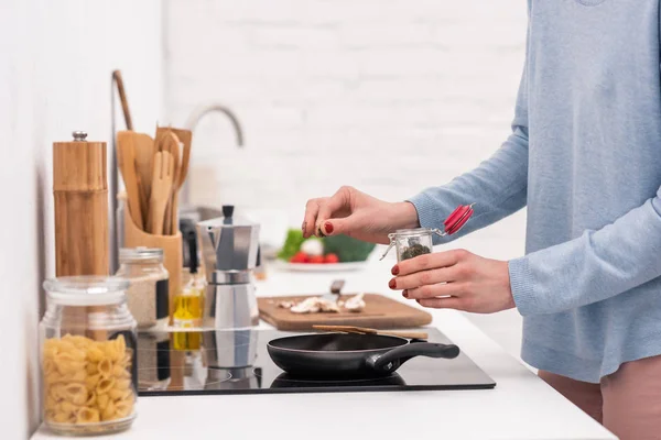 Обрізаний знімок жінки, що наливає спеції на їжу, готуючи на сковороді — стокове фото