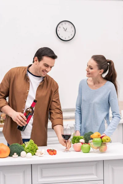 Feliz pareja adulta con vino tinto cocinando juntos en la cocina - foto de stock