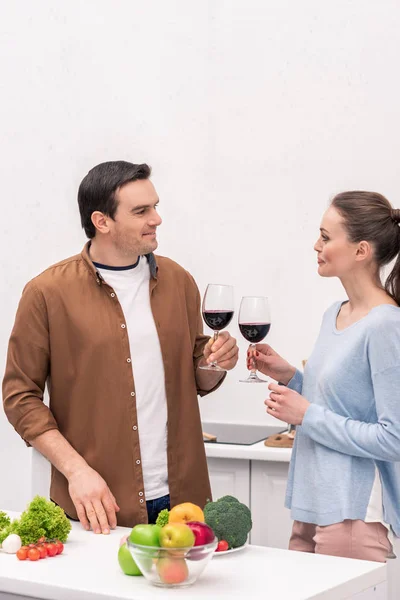 Schönes erwachsenes Paar klimpert bei der Zubereitung des Abendessens in der Küche mit Weingläsern — Stockfoto