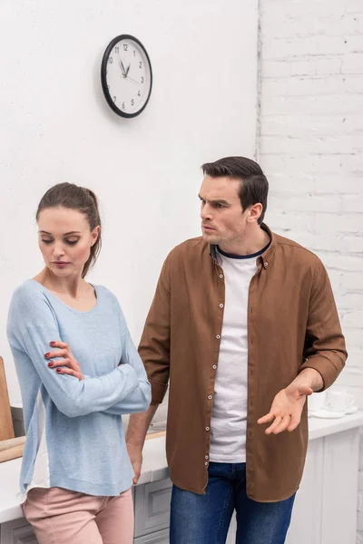 Angry adult man looking at wife while she ignoring him after quarrel at kitchen — Stock Photo