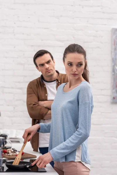 Сердитий дорослий чоловік дивиться на дружину, поки вона ігнорує його після суперечки на кухні — стокове фото